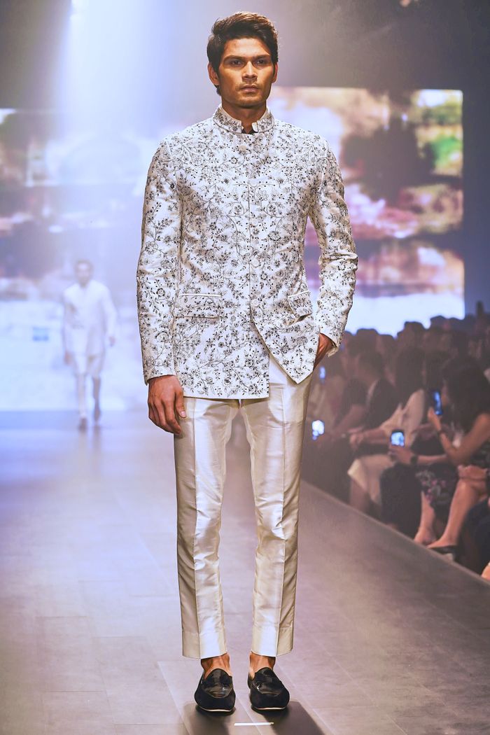 our-vission Stylish man in floral suit walking on a runway during a fashion event.