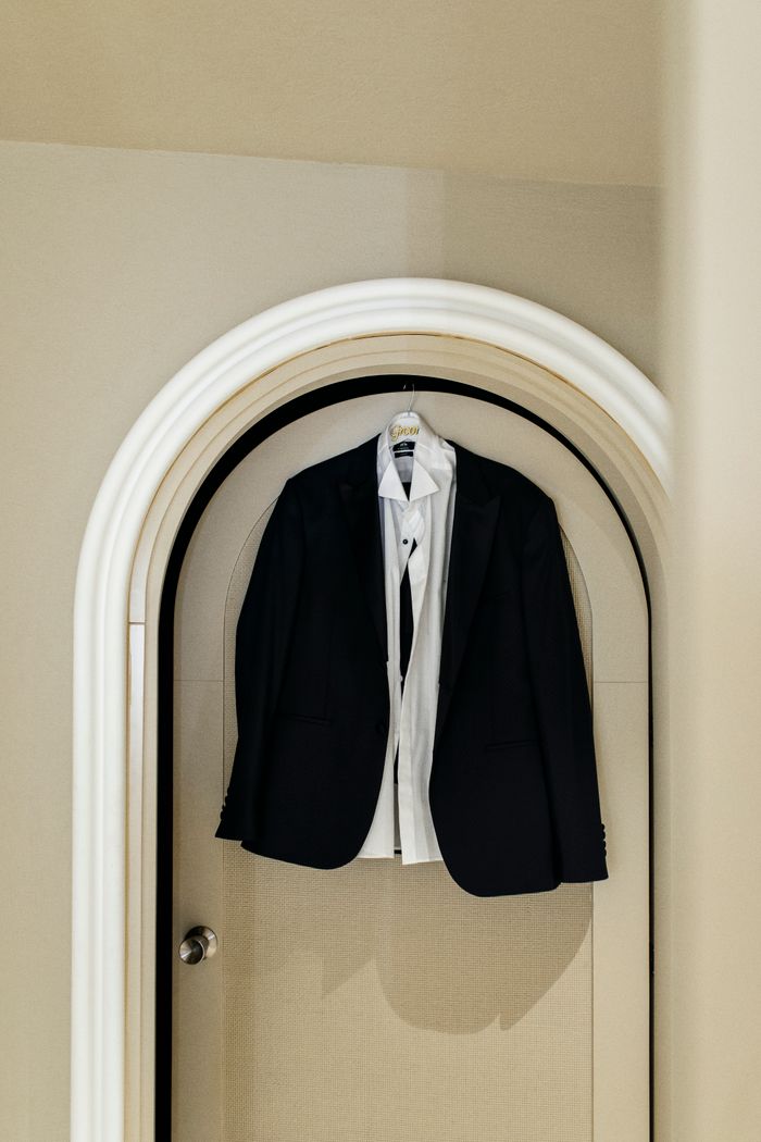 Classic black suit and white shirt hanging on an arched door, showcasing elegance and sophistication.