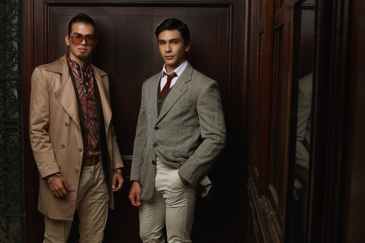 Two men in fashionable suits posing indoors, showcasing elegance and style.