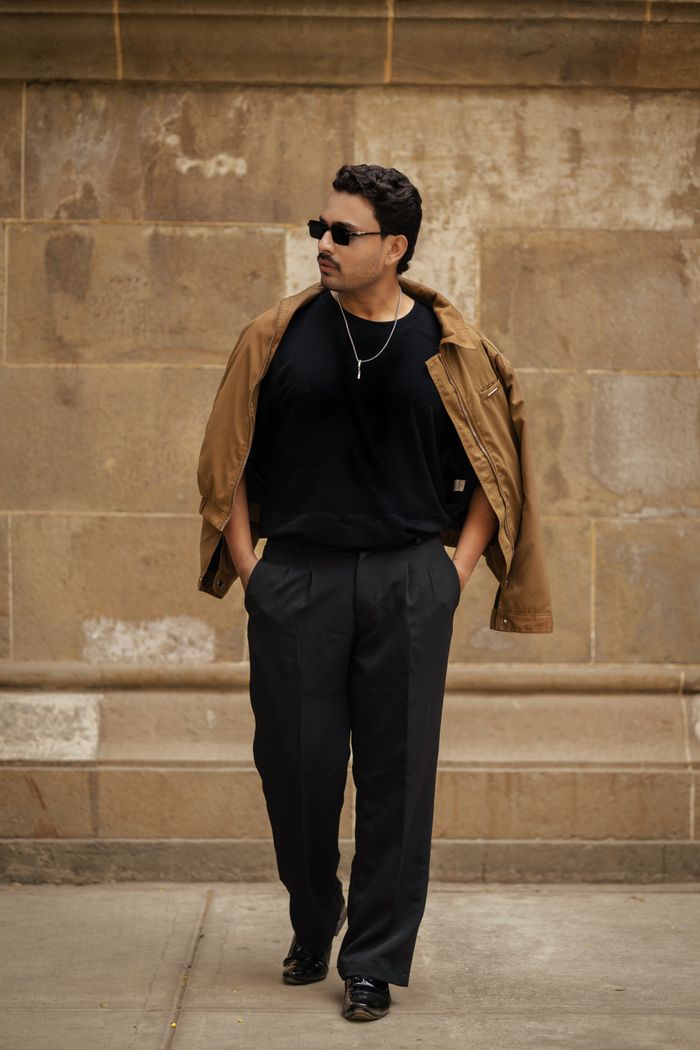 Stylish man walking in a city, wearing sunglasses and casual attire.