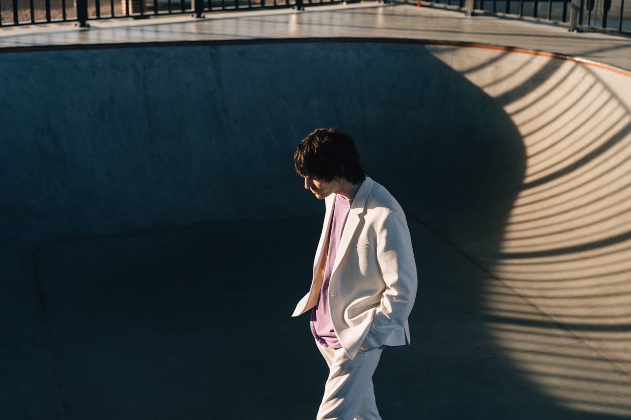 Fashionable man in white blazer walking in a sunlit skate park bowl.